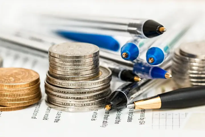 Pilas de monedas junto a bolígrafos